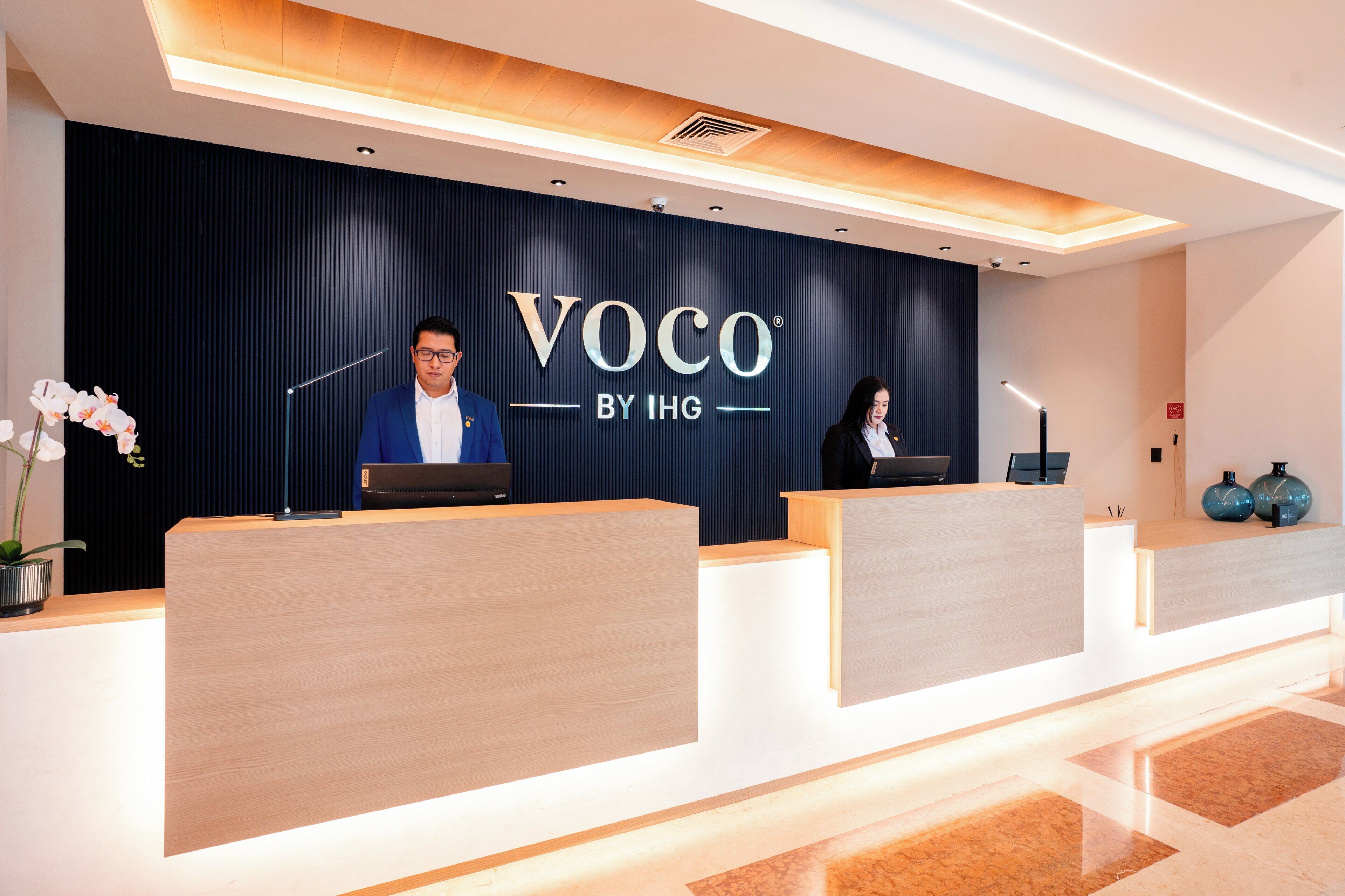 Un mostrador de recepción con acabado en madera oscura y un letrero que dice 'VOCO BY IHG'.