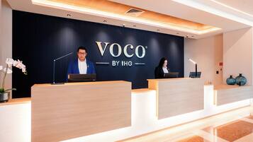 Un mostrador de recepción con acabado en madera oscura y un letrero que dice 'VOCO BY IHG'.