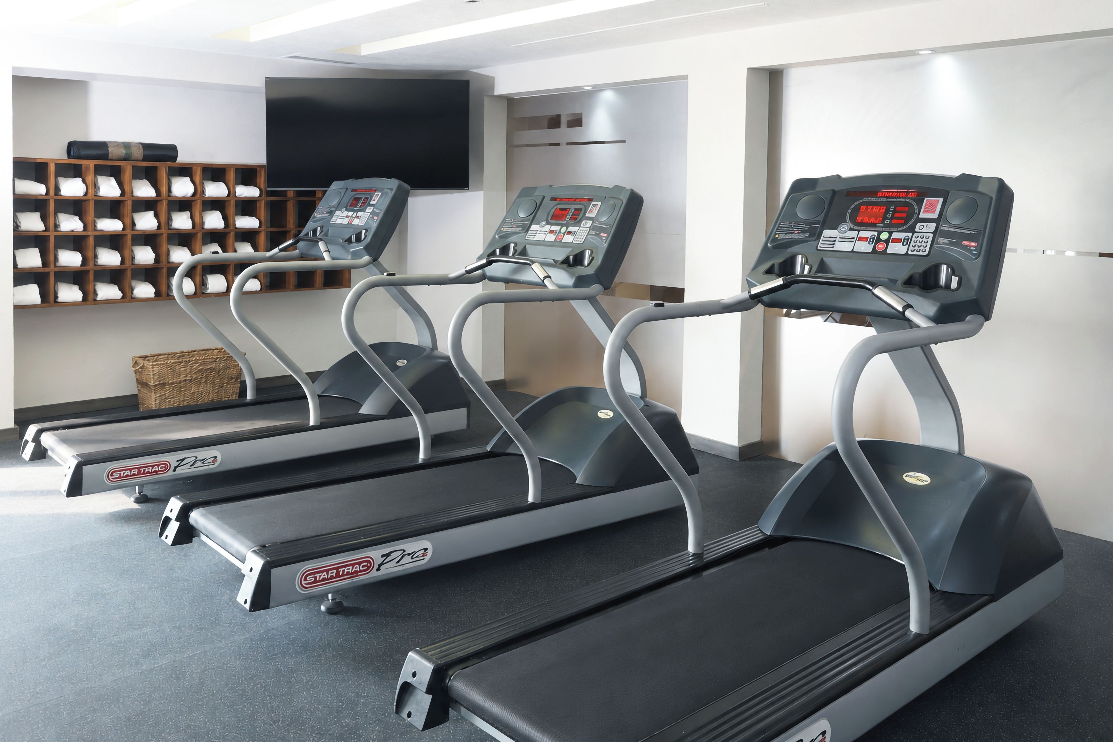 Tres cintas de correr en una sala con un televisor de pared y un perchero.