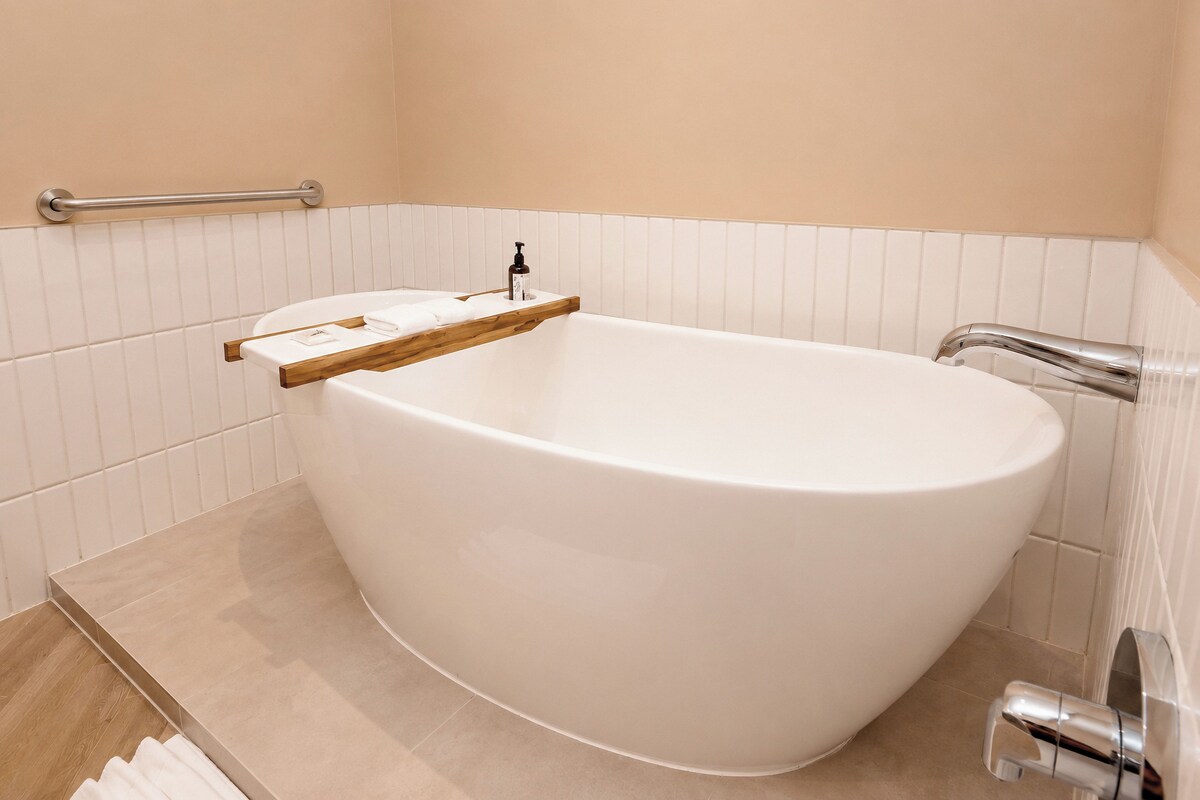 Un baño moderno con una bañera independiente, un estante de madera y un pasamanos.