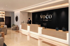Bancada de recepção com fundo preto e o texto 'VOCO BY IHG'.