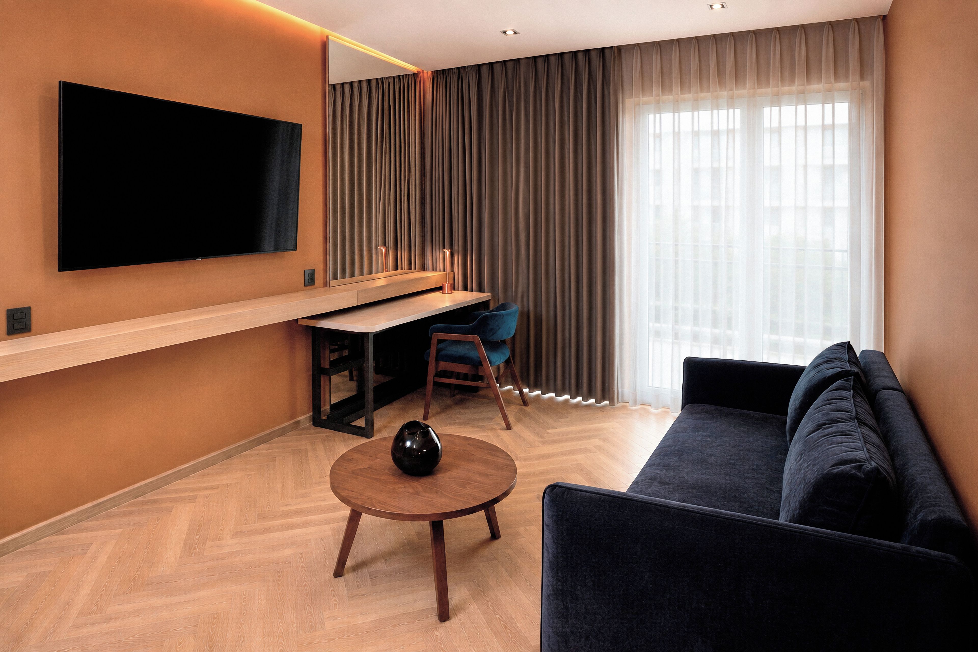 A modern living room with a flat-screen TV, a desk, a chair, a sofa, and a coffee table.