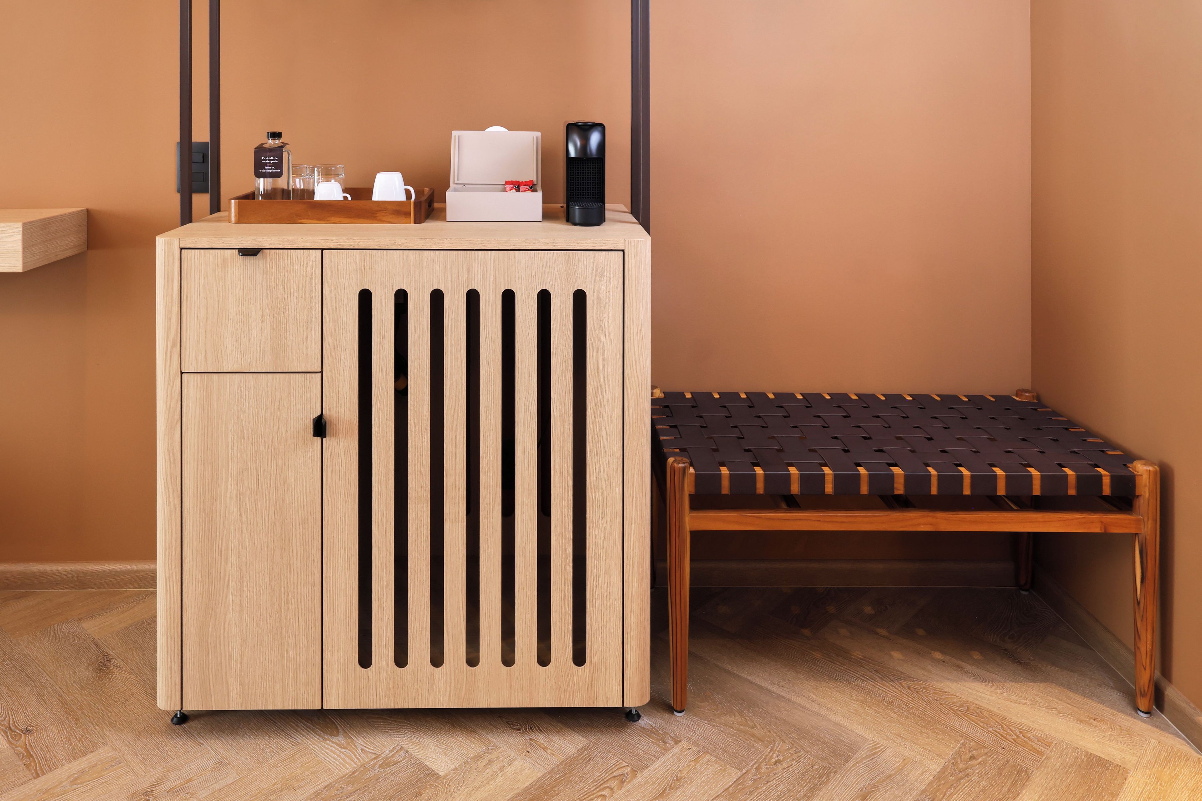 A wooden cabinet with a drawer, a small table with a woven seat, and a coffee machine on top.