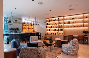 Un moderno espacio de bar con asientos y una exhibición de botellas y copas diversas.