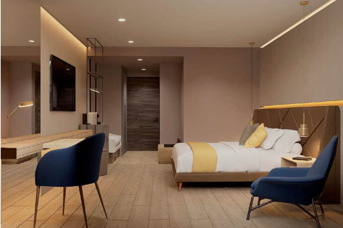 Een moderne hotelkamer met een bed, twee stoelen, een bureau, een spiegel en een wandplank.