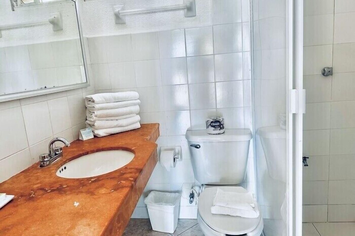 Un baño con tocador de madera, inodoro y un pequeño cubo de basura.