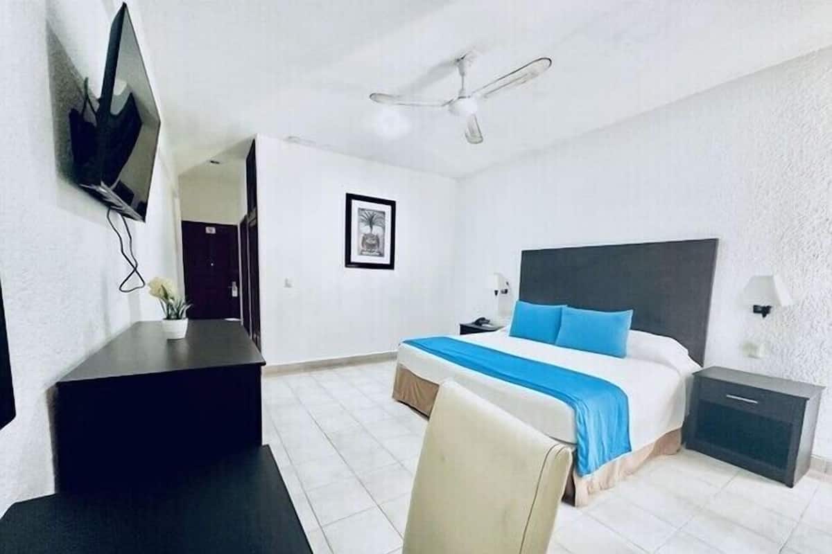 A hotel room with a bed, a desk, a chair, a TV, and a ceiling fan.