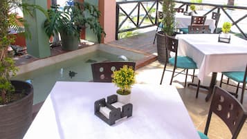 An outdoor patio area with tables and chairs, a small water feature, and potted plants.
