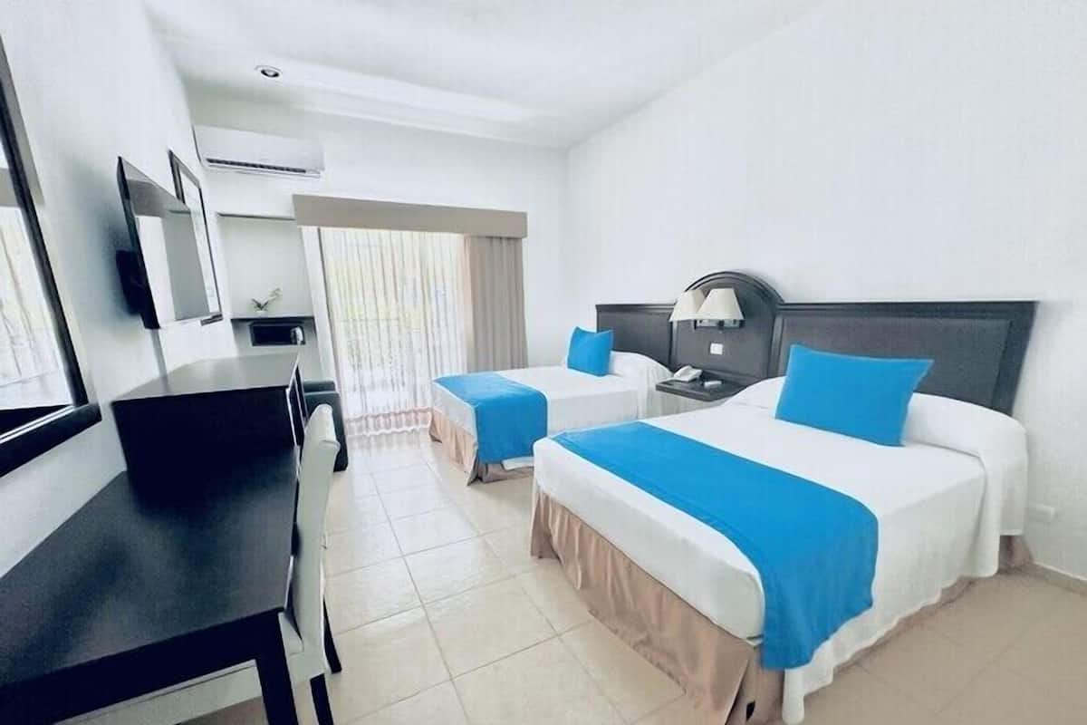 A hotel room with two beds, a desk, a chair, a TV, and an air conditioning unit.