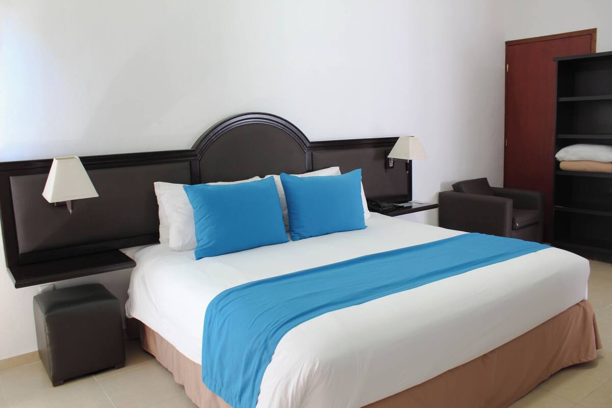 A hotel room with a bed, two bedside tables, a nightstand, a chair, a wardrobe, and a door.