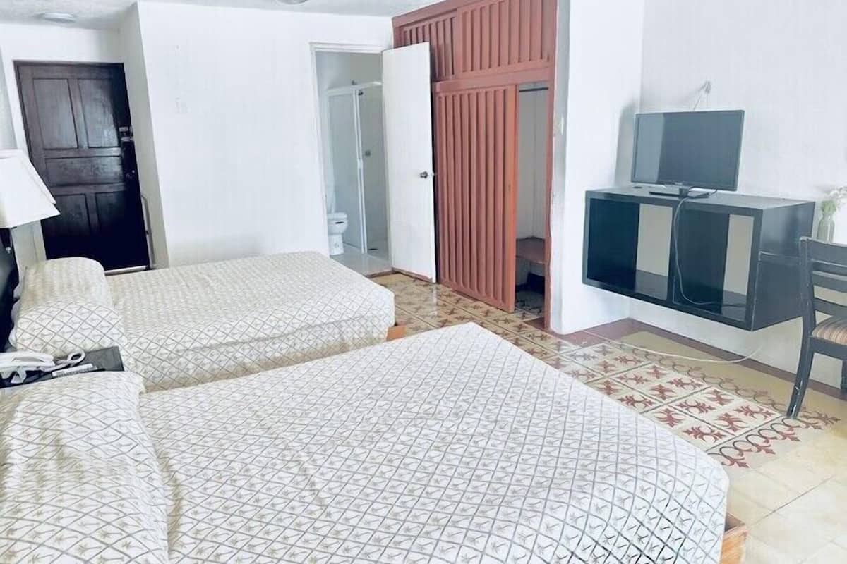 A hotel room with two beds, a desk with a television, a wardrobe, and a ceiling fan.