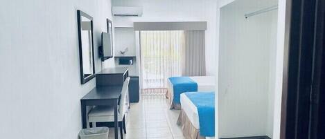 A hotel room with a desk, two beds, a trash bin, and a window with curtains.