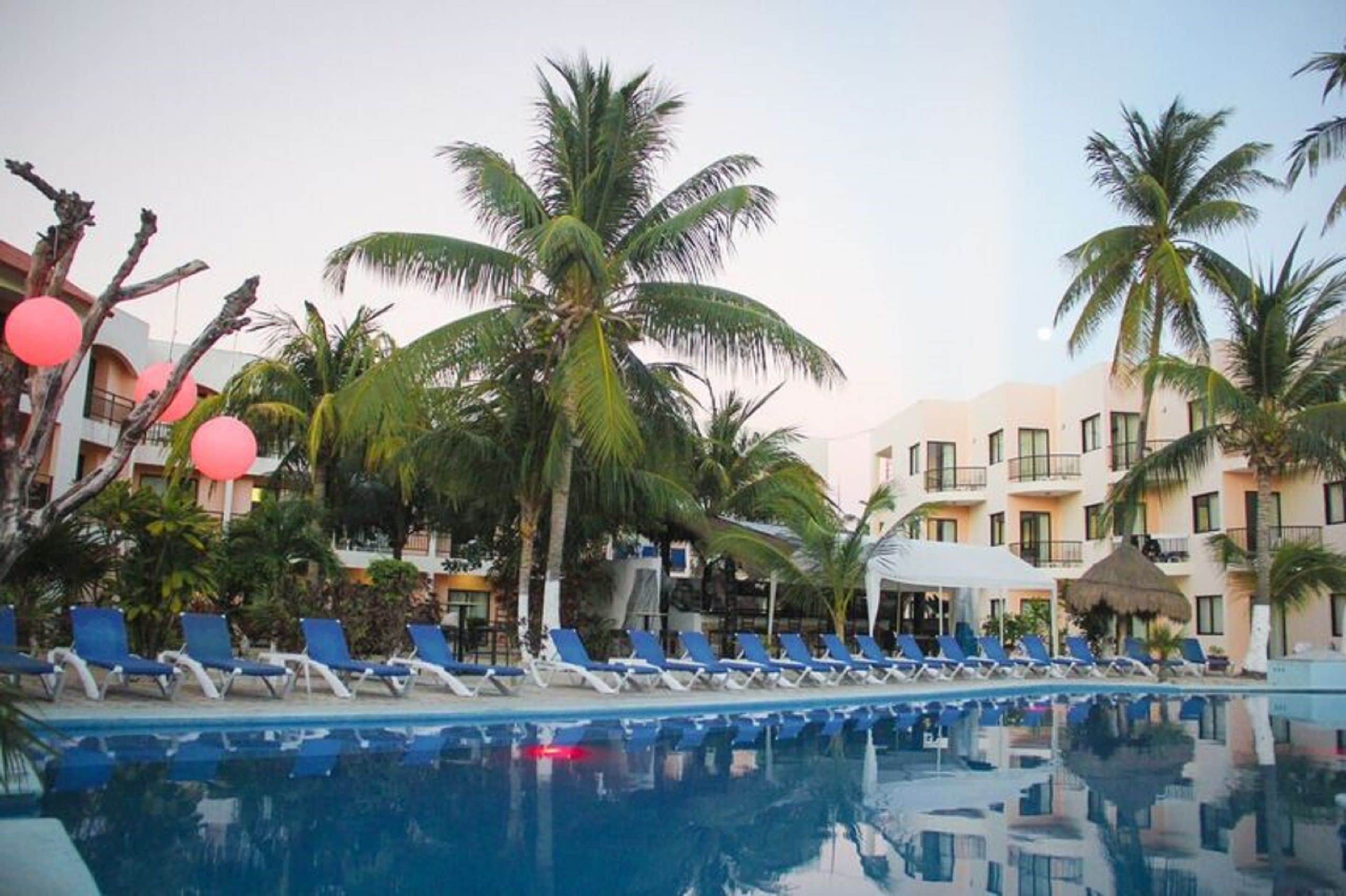 A poolside area with lounge chairs, palm trees, and a building with balconies.