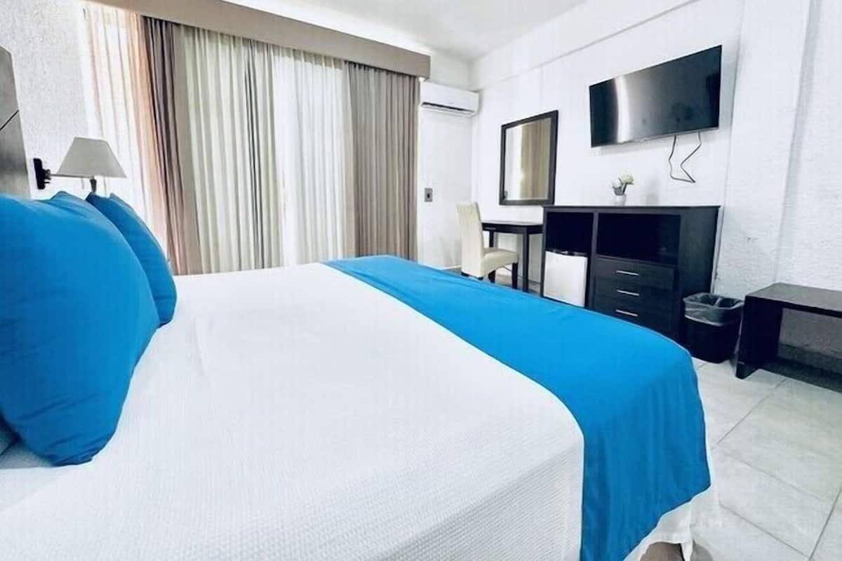 A hotel room with a large bed, a desk, a chair, a TV, and a window with curtains.