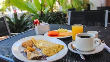 Una mesa de comedor con un plato de comida, una taza de café y un vaso de jugo de naranja.