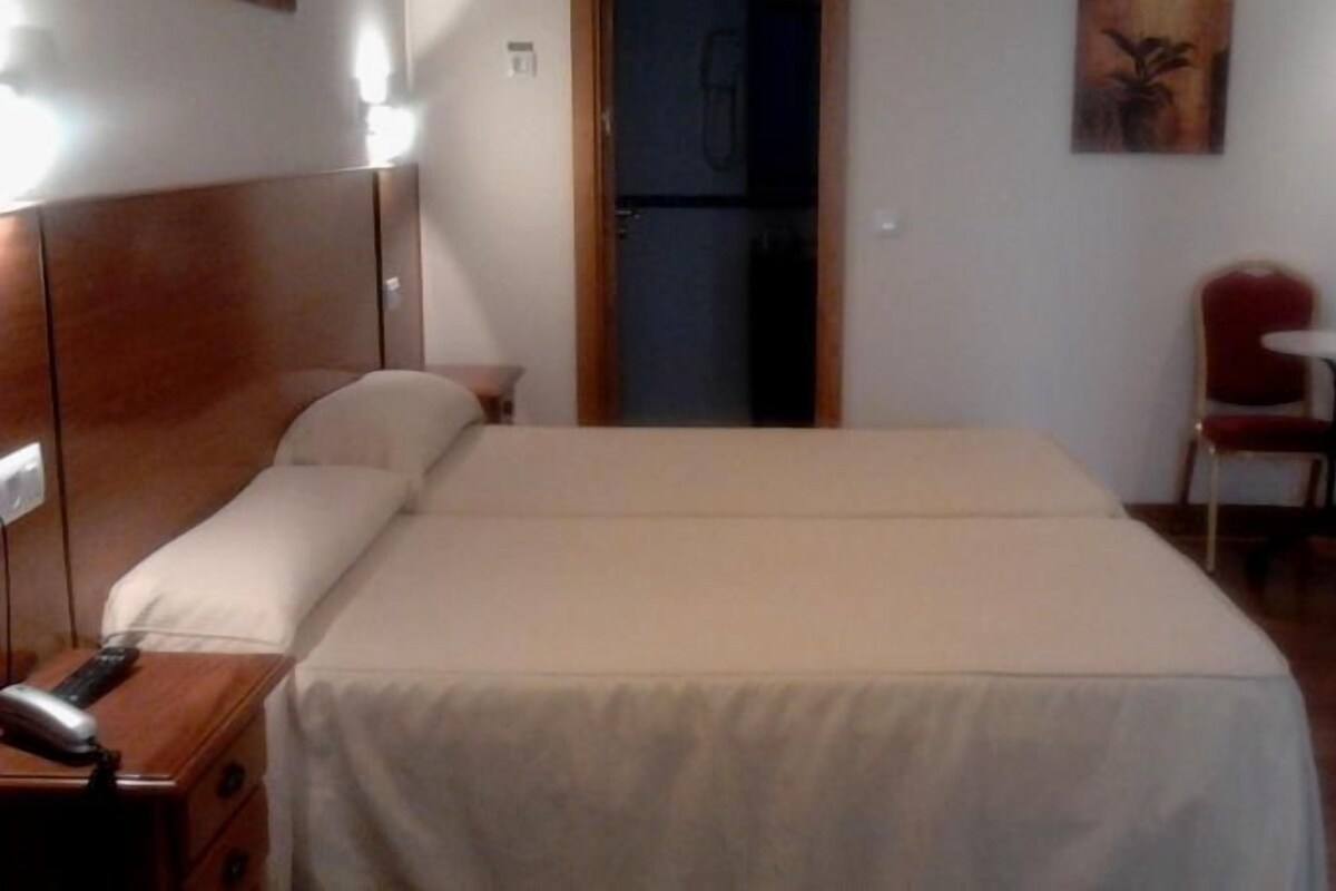 A hotel room with a bed, a desk with a telephone, a chair, and a small table.