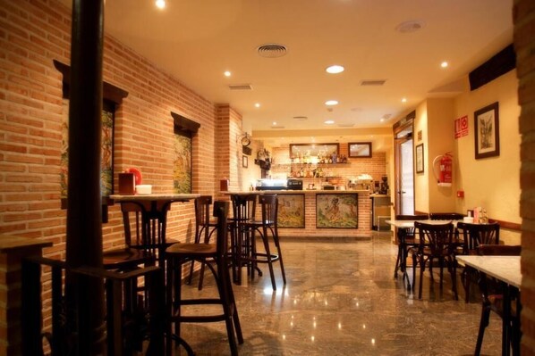 A restaurant with brick walls, wooden tables and chairs, a bar area, and a polished floor.