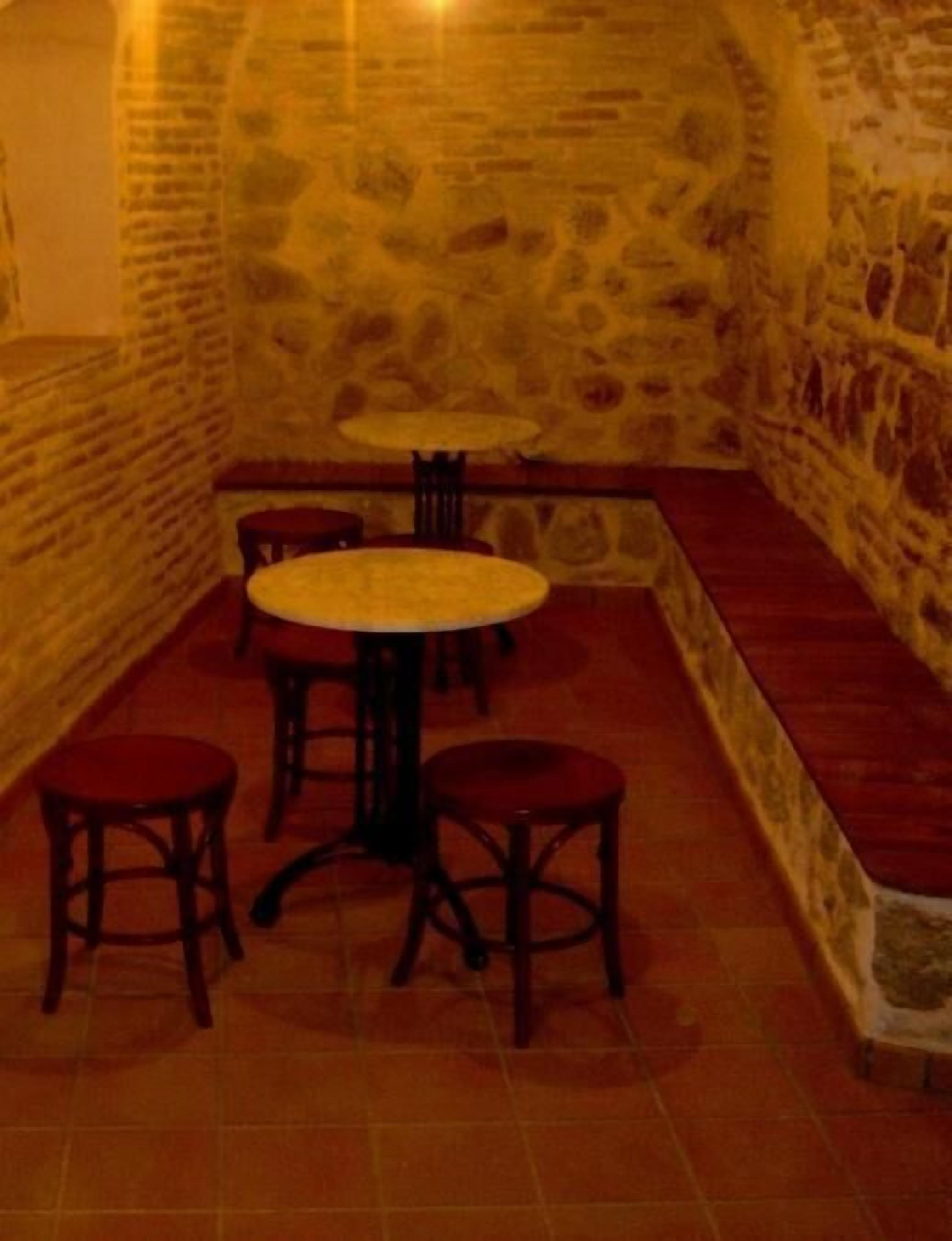 A stone-walled room with a low bench and four wooden tables and chairs.