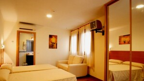 A hotel room with two beds, a sofa, a mirror, and a television. - Hotel Eurico (Toledo)
