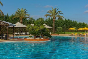 A swimming pool with lounge chairs and umbrellas, surrounded by palm trees and greenery.