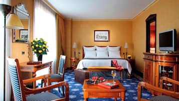 Ein Hotelzimmer mit einem Bett, einem Schreibtisch mit Lampe, einem Sessel, einem Tisch mit Buch und einem Weinglas sowie einem Fernseher.