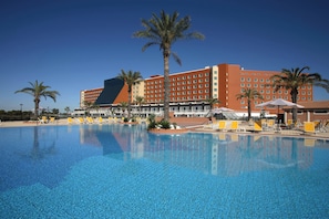 Un hotel con una piscina grande, palmeras y sillas de descanso amarillas.
