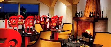 A restaurant with red chairs, yellow cushions, and a brick fireplace.