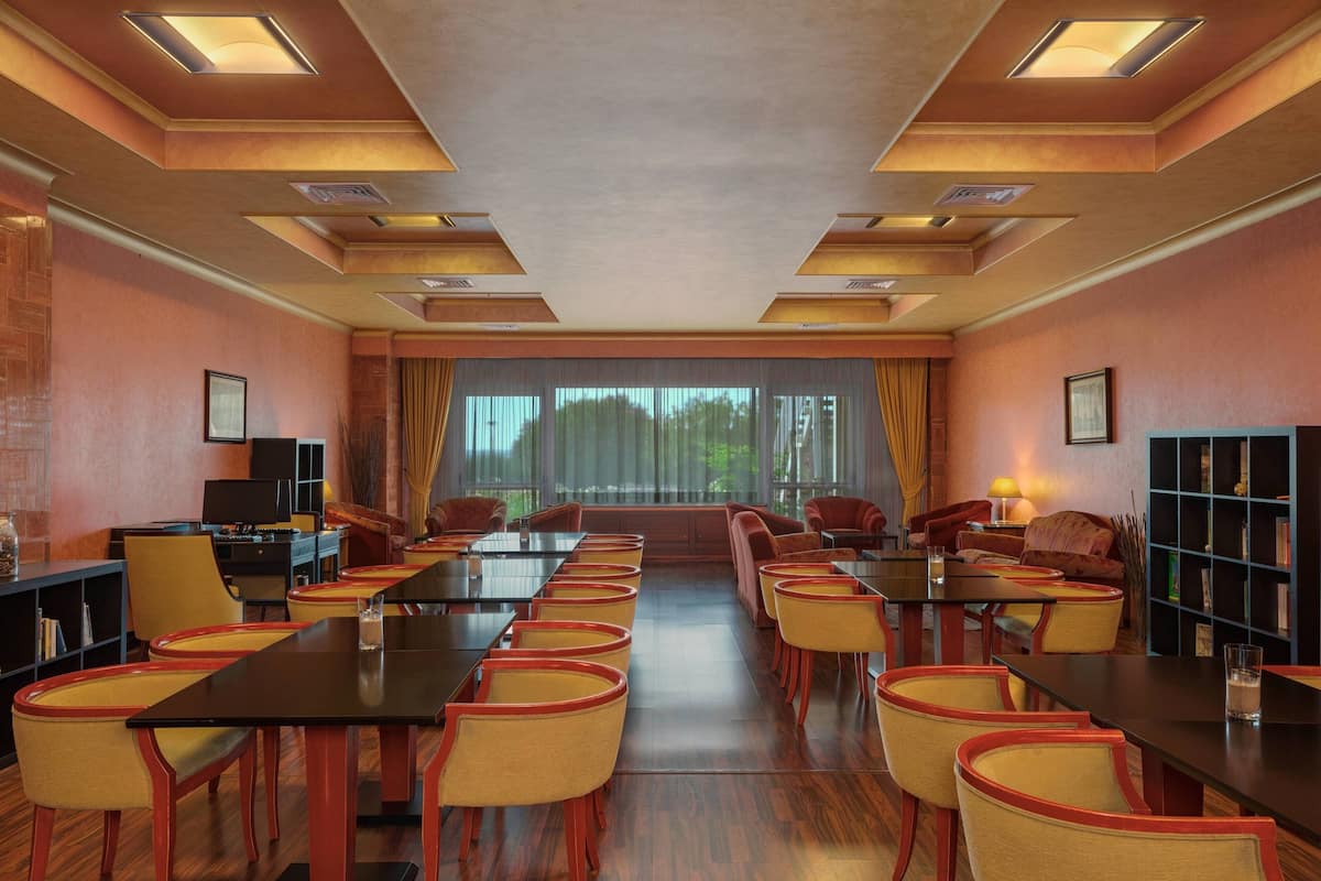 A conference room with long tables and chairs, a bookshelf, and a large window with curtains.
