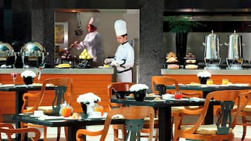En restaurant med træstole og borde, en kok der tilbereder mad, samt forskellige retter udstillet i disken.