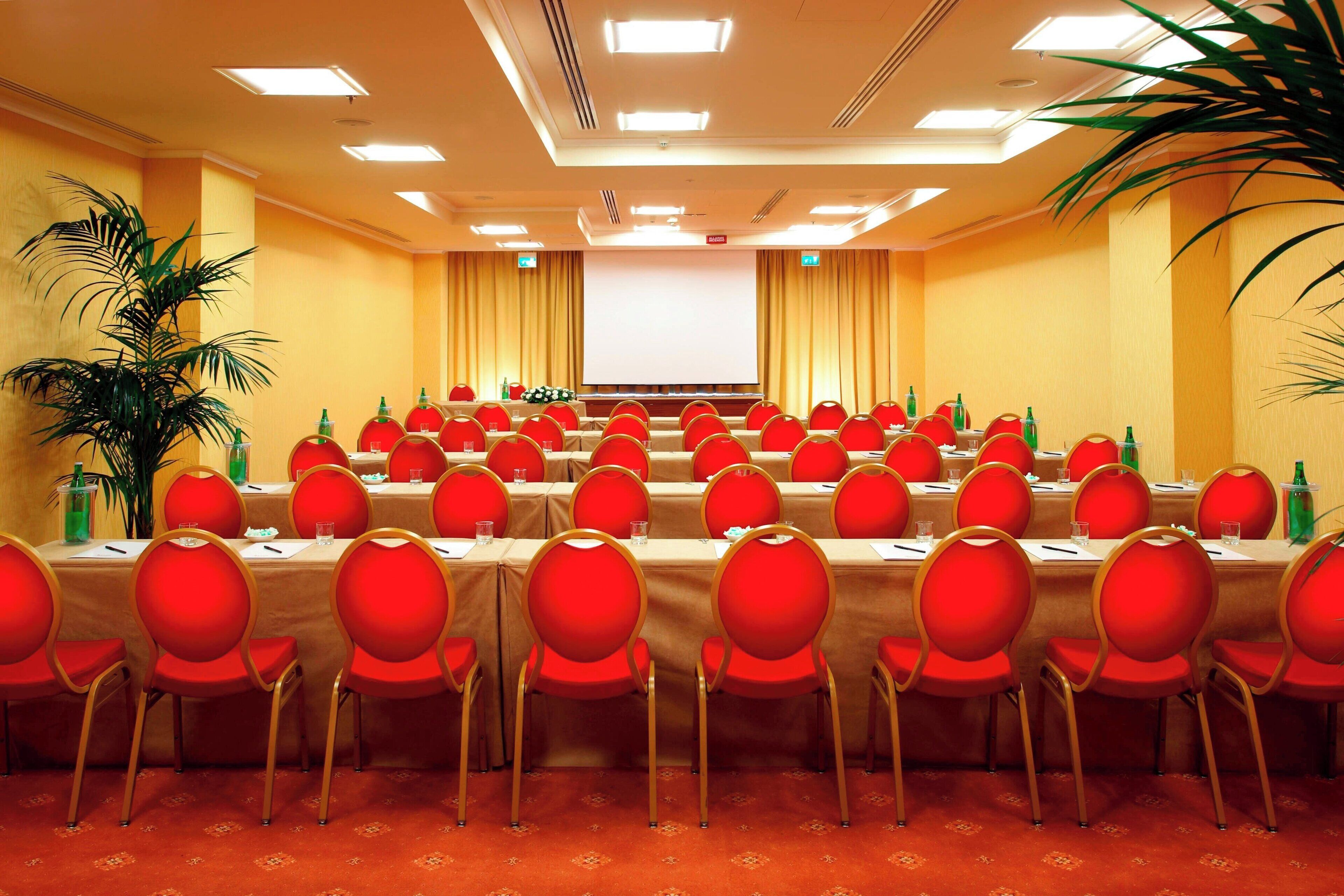 A conference room with multiple tables and red chairs, equipped with microphones and water bottles.