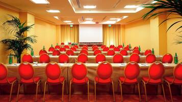A conference room with multiple tables and red chairs, equipped with microphones and water bottles.