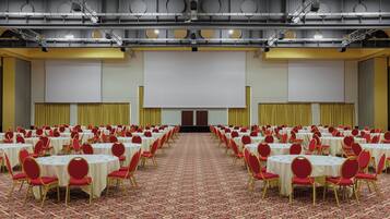 Un'ampia sala conferenze con file di tavoli e sedie, un palco e un pavimento rivestito di moquette.