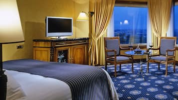 Camera d'albergo con un letto grande, una televisione, due poltrone, un tavolino e vista sulla città illuminata.