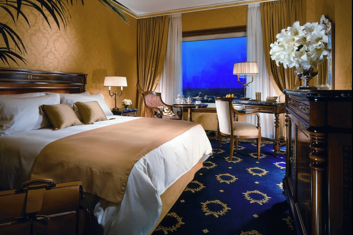 A hotel room with a large bed, a desk, a chair, and a view of the night sky.