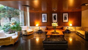 A spacious lobby with a wooden ceiling, a central coffee table with a vase of flowers, leather sofas, and a seating area with a view of greenery outside. - 474 Buenos Aires Hotel (Buenos Aires)