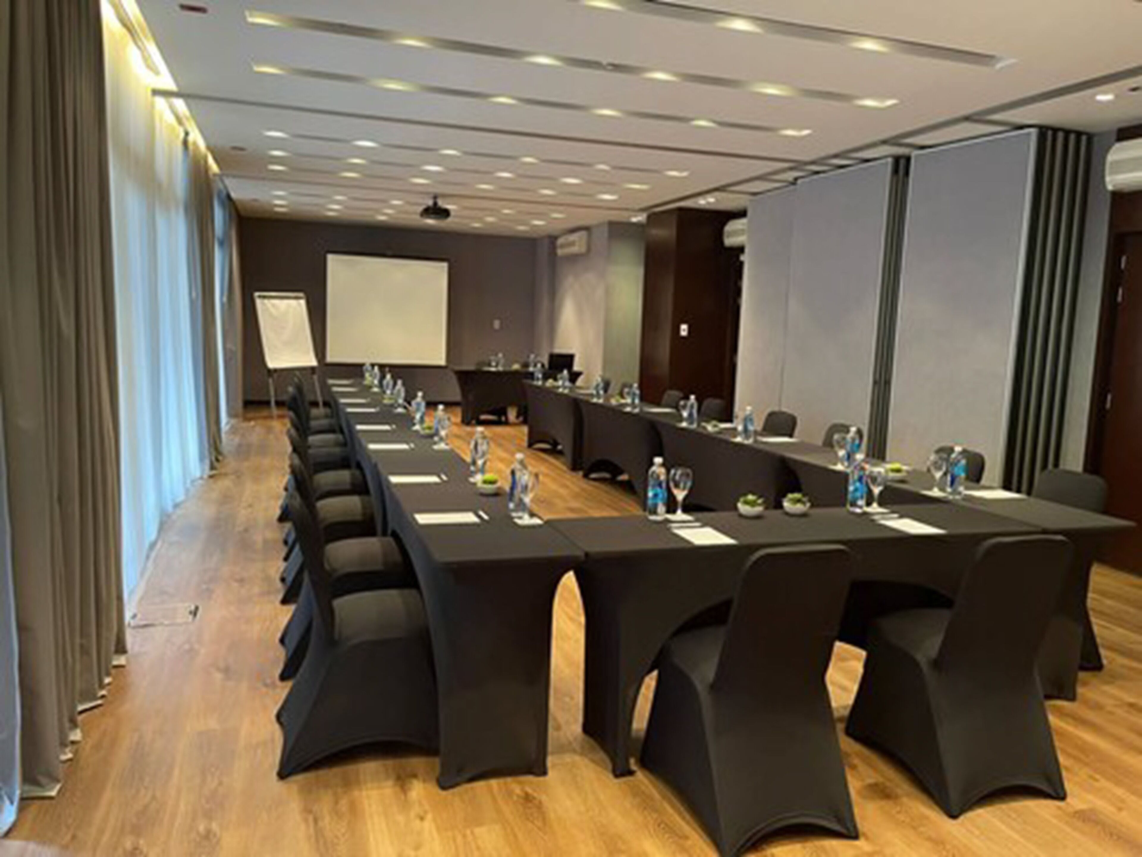 Un salón de conferencias con una larga mesa, sillas negras y una pantalla para proyector.