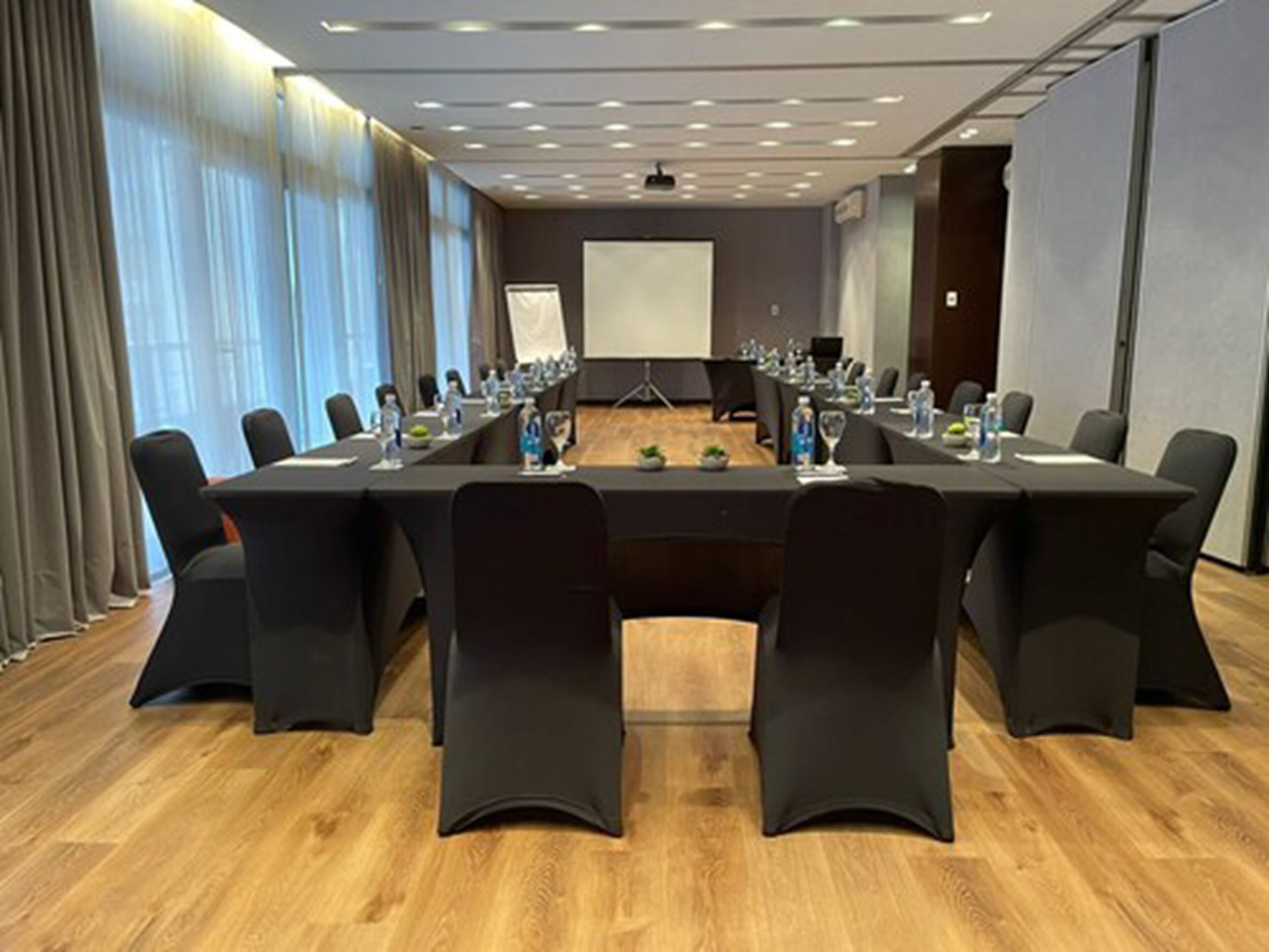 A conference room with a long table, black chairs, and a projector screen.