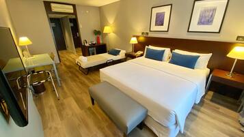 Habitación de hotel con una cama grande, un escritorio, una silla, un banco y dos mesitas de noche con lámparas.