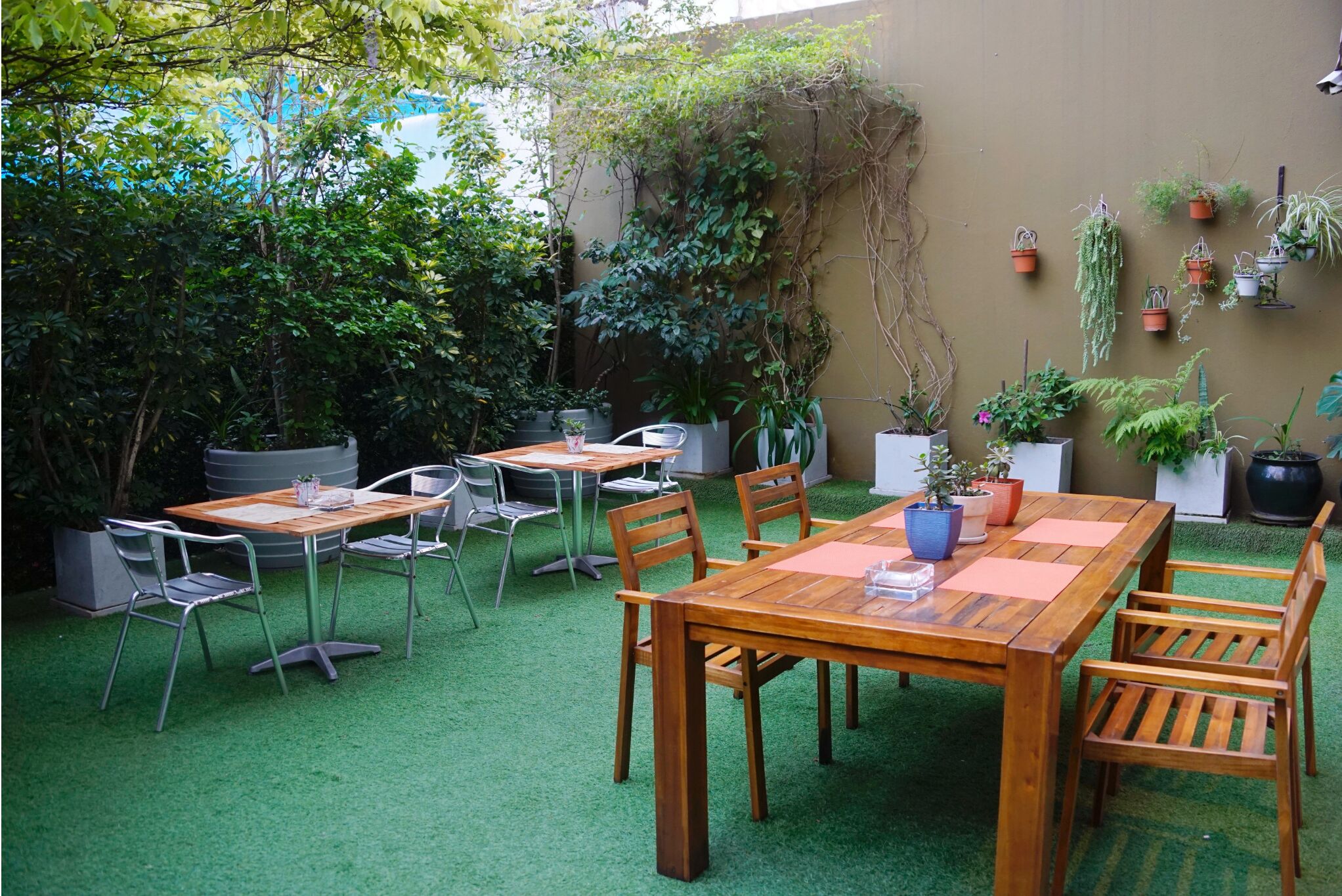 Een terras buiten met een houten tafel en stoelen, omringd door potplanten en groen.