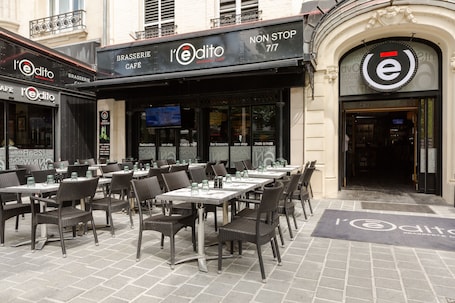 An outdoor café with tables and chairs, a sign reading "l'edito," and a "NON STOP 7/7" sign above the entrance.