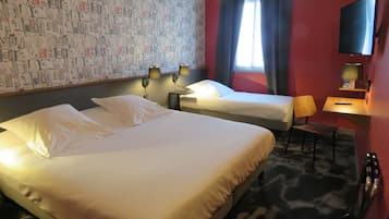 A hotel room with two beds, a desk, a chair, a TV, and a patterned wall.