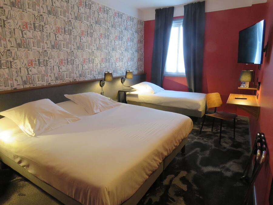 A hotel room with two beds, a desk, a chair, a TV, and a patterned wall.