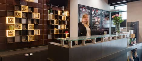 A modern bar area with a glass counter, illuminated number boxes on the wall, and a menu board.