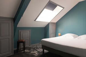Una camera da letto con finestra sul tetto, un letto, un comodino e una sedia.