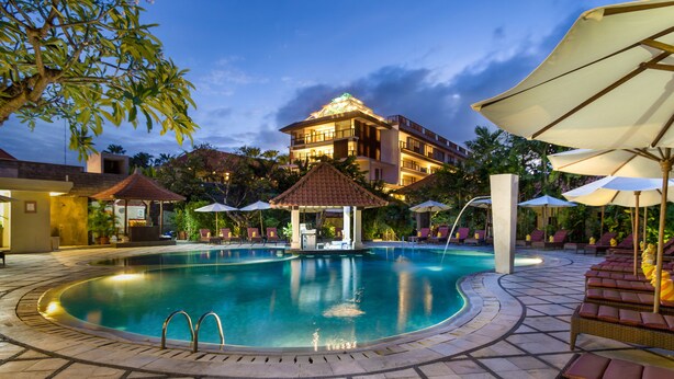 A swimming pool with a gazebo, lounge chairs, and umbrellas. - Hotel Puri Raja (Legian)