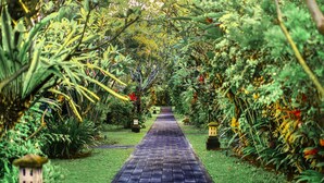 A garden pathway with a brick surface, surrounded by lush greenery and small decorative lanterns. - Hotel Puri Raja (Legian)