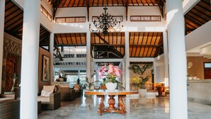 A spacious lobby with high ceilings, a chandelier, and a central round table with potted plants. - Hotel Puri Raja (Legian)