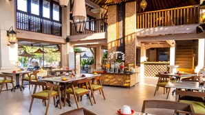 A spacious dining area with multiple tables and chairs, a central bar, and large windows allowing natural light. - Hotel Puri Raja (Legian)