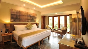 A spacious bedroom with a large bed, a desk with a chair, a television, and a window with curtains. - Hotel Puri Raja (Legian)