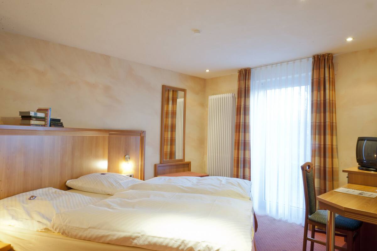 A hotel room with a bed, a desk with a television, and a window with curtains.